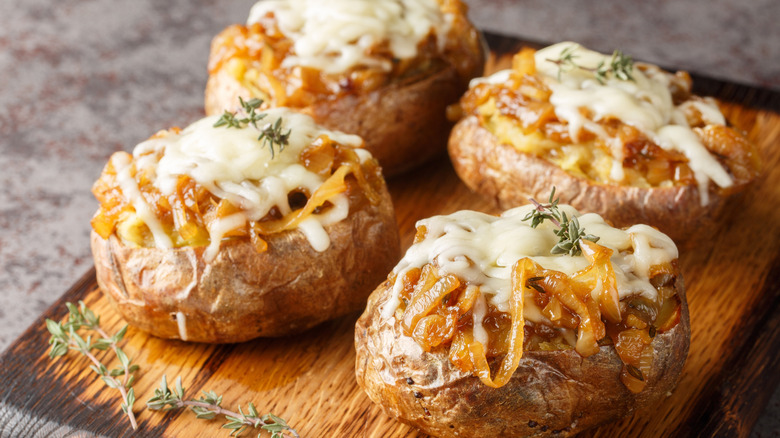 Four French onion baked potatoes on a wooden board