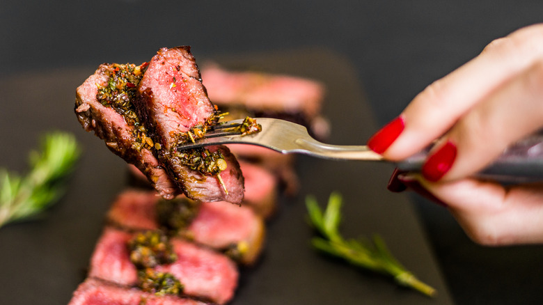 Hand holding fork of sliced cooked steak with chimichurri