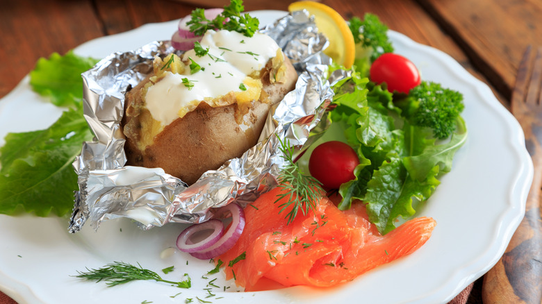 A baked potato topped with sour cream and a side of smoked salmon