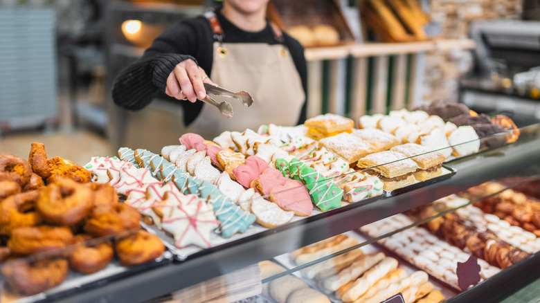 female bake shop clerk with tongs grabbing baked treats from display at bakery