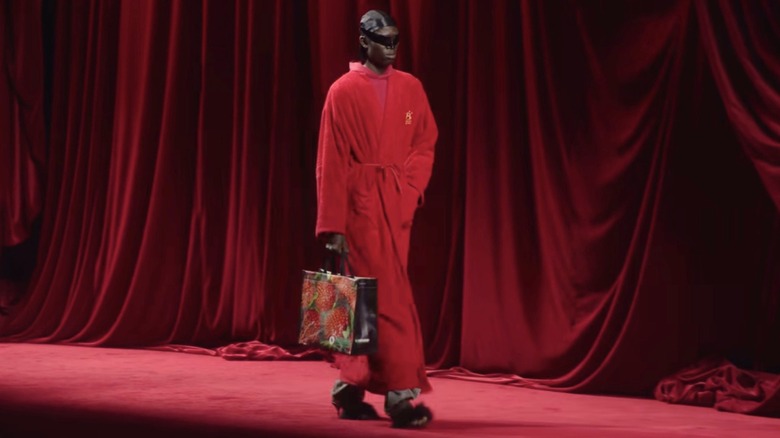 A Balenciaga model walks the runway with a plastic tote bag