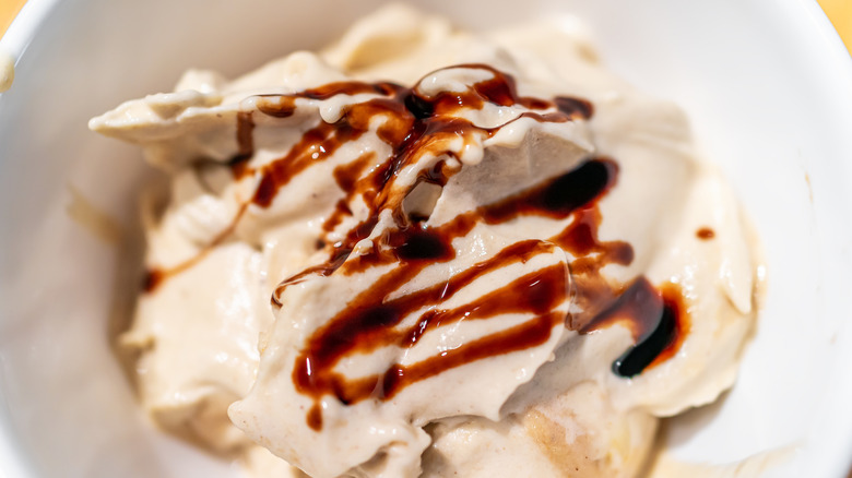 White ice cream in a white bowl with dark brown balsamic vineger drizzled on top