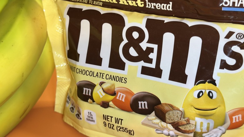 Close up of a bag of M&M's banana nut bread next to bunch of bananas
