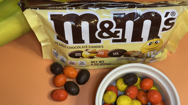 Close up of a bag of Banana Nut Bread M&Ms behind loose candies and ramekin of the candies