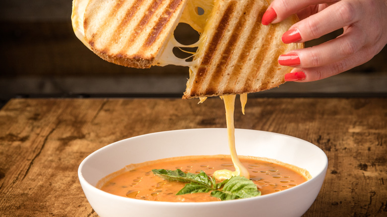 Hands pulling apart a grilled cheese over a bowl of tomato soup