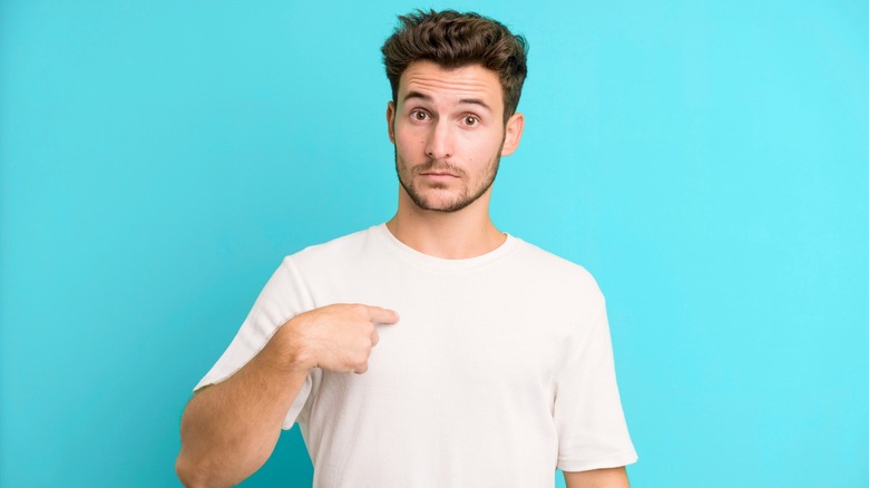 Young man pointing to himself as if asking, who me?