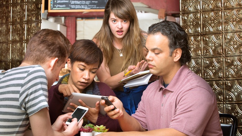 Customers on phones ignoring a staff member in a cafe or coffee house