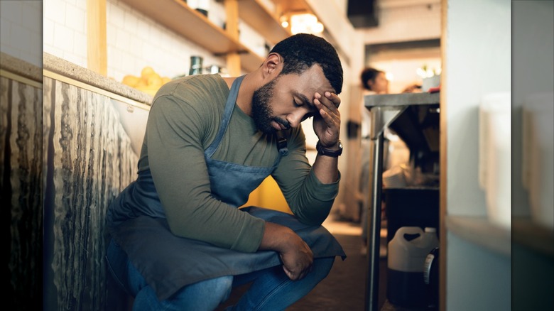 Staff member in a coffee shop squatting on the floor and holding head in hands