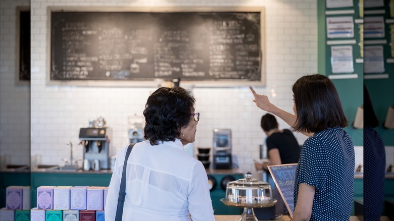 Woman pointing at something on a chalkboard menu in a coffee shop.
