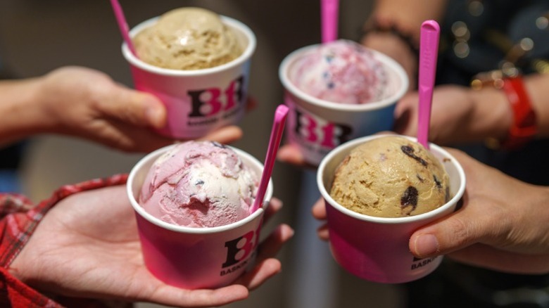 Four hands holding four cups of Baskin-Robbins ice cream.