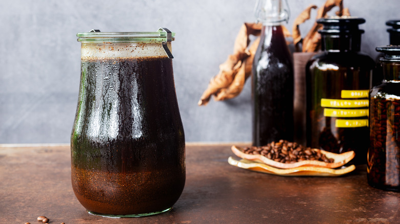 A jar of homemade cold brew sits on a counter near other jars and a plate of coffee beans