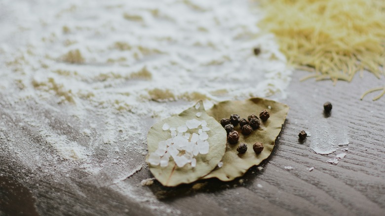 Dried bay leaves pictured with various spices, salt, and pepper