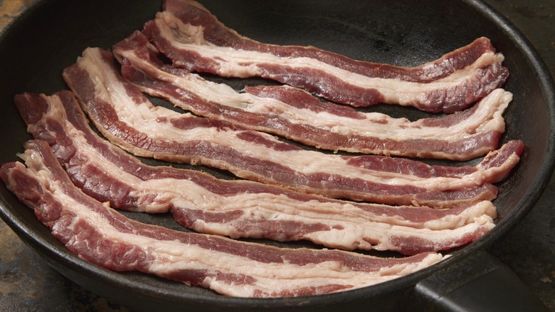 Raw beef bacon strips in frying pan