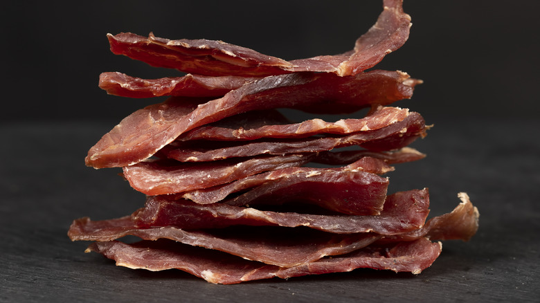 Thin pieces of beef jerky piled on top of one another in front of a black background