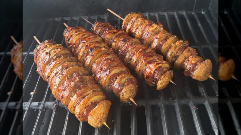 Four beef and potato kebabs cooking on a grill