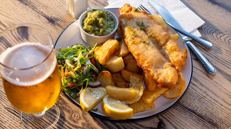 A plate of battered fish on a table with a glass of beer