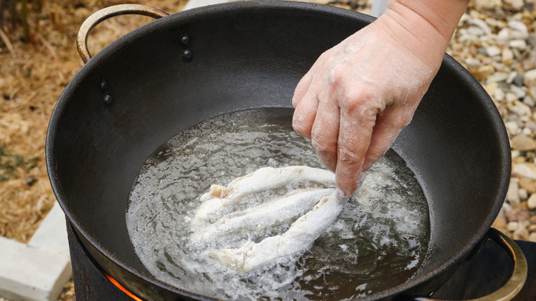 A hand frying flour-coated sardine fish in oil