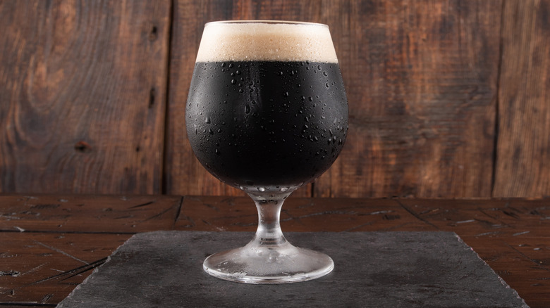Glass of dark beer, sweating in its glass, on a wooden background