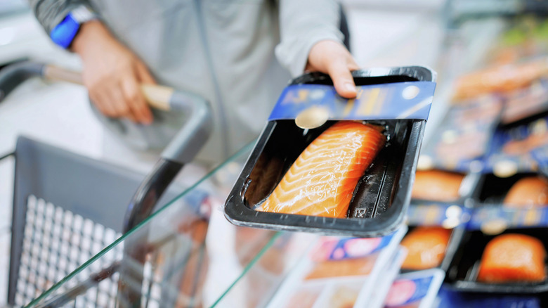 A person picking up pre-packaged salmon fillet at a grocery store