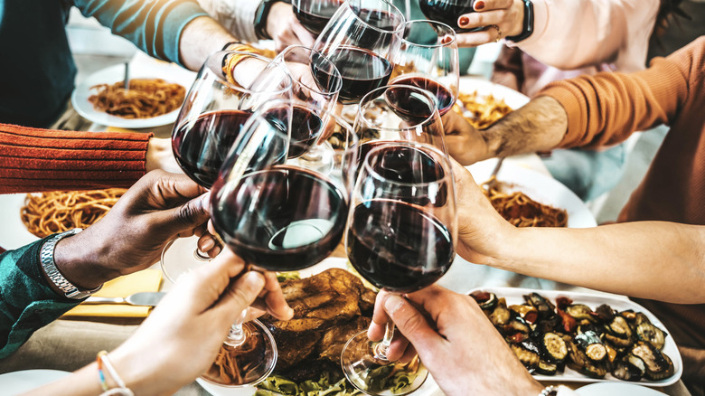 Wine glasses filled with red wine being toasted above a table laden with Italian dishes