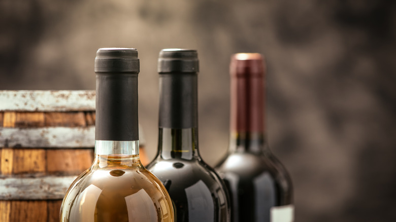 Three sealed bottles of wine with a wine barrel behind them