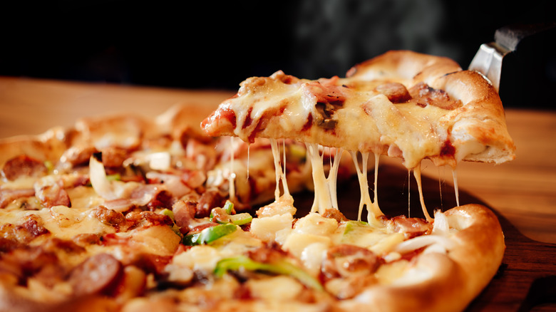 A slice of cheesy pizza getting pulled away from the rest on a spatula.