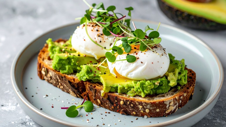 Avocado toast with poached eggs and micro greens on a gray plate