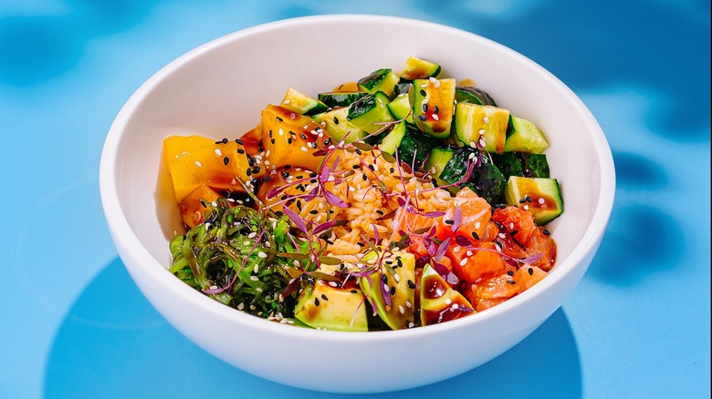 White bowl of tuna poke served with vegetables and toasted sesame seeds