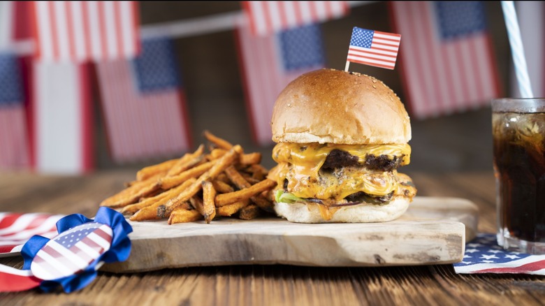 Double decker burger and fries on a wooden slab garnished with an American flag