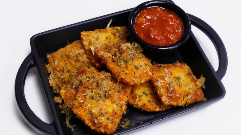Toasted ravioli with marinara sauce on a black platter