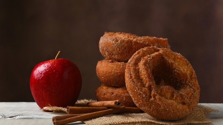 A stack of apple cider Donuts with cinnamon sticks and an apple on a burlap piece of material