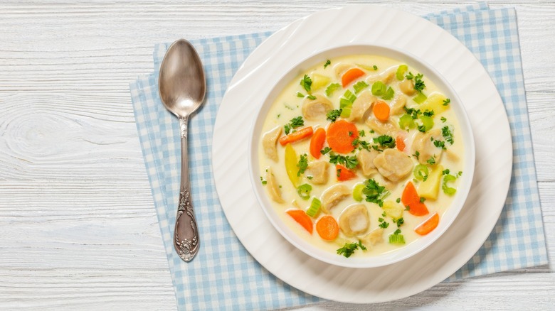 Knoephla soup in a white bowl on a blue checkered napkin