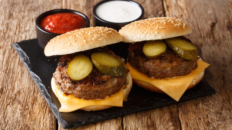 Two Oklahoma fried onion burgers with cheddar cheese and pickles served on black slate