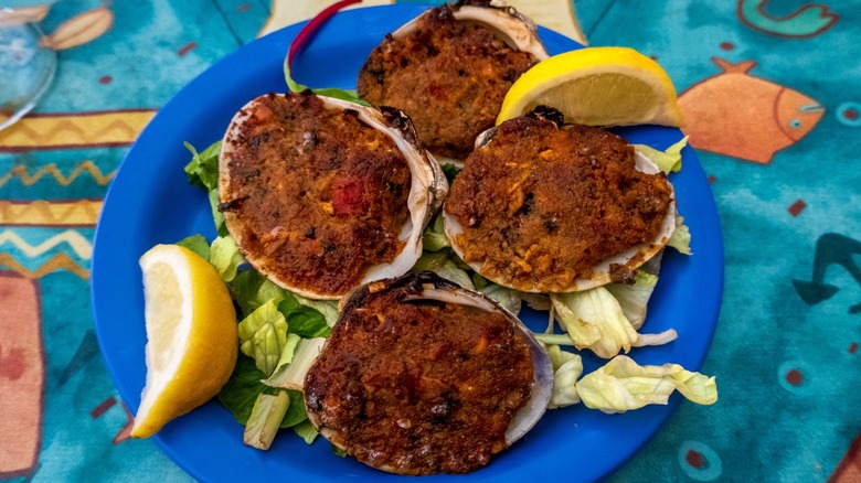 A blue plate of baked stuffed clams garnished with lettuce and lemon wedges