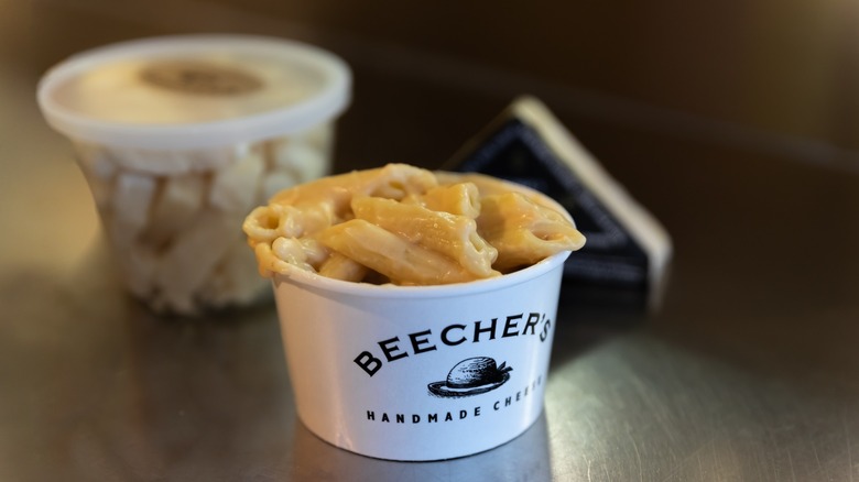 Mac and cheese in a Beecher's to-go container on a wooden surface