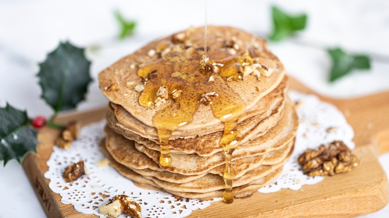Stack of buckwheat cakes on a lace doily coated with syrup and walnuts
