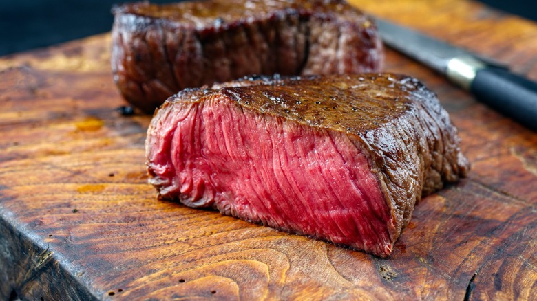 Rare bison steak cut in half sitting on a wooden cutting board