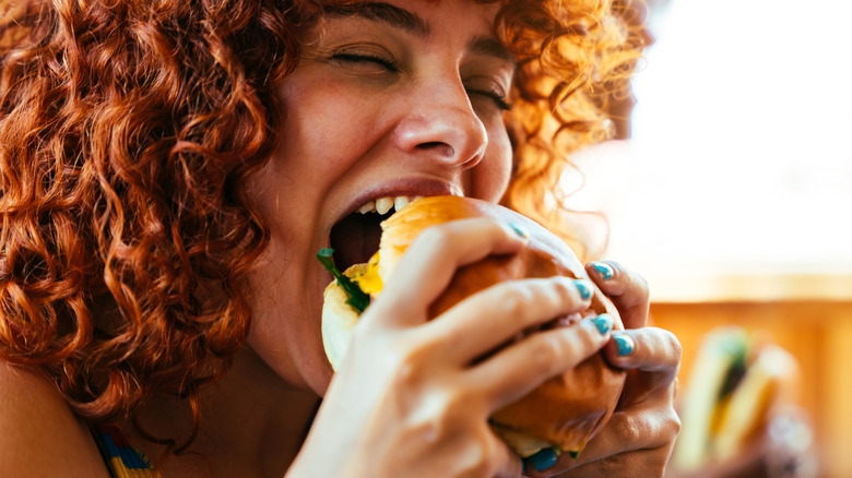 Close-up of a young woman eating a burger with her eyes closed