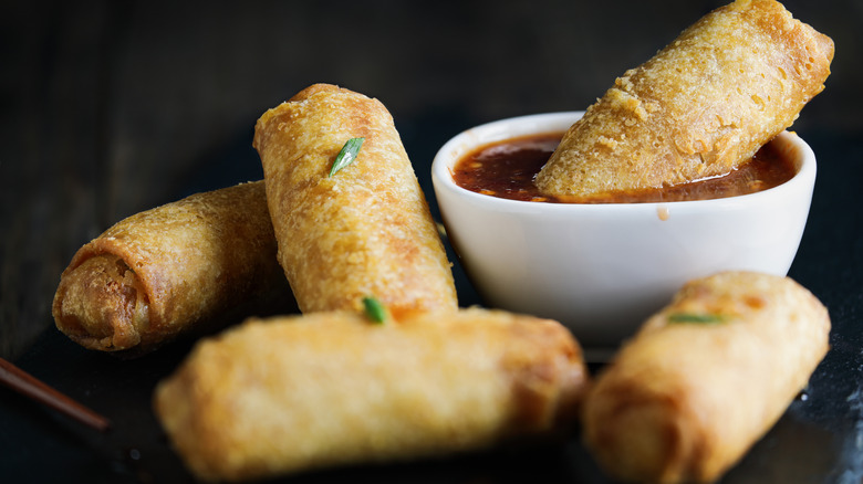 Egg rolls in sweet and sour sauce over a dark rustic table.