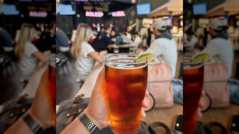 A hand holding a glass of beer in a busy area