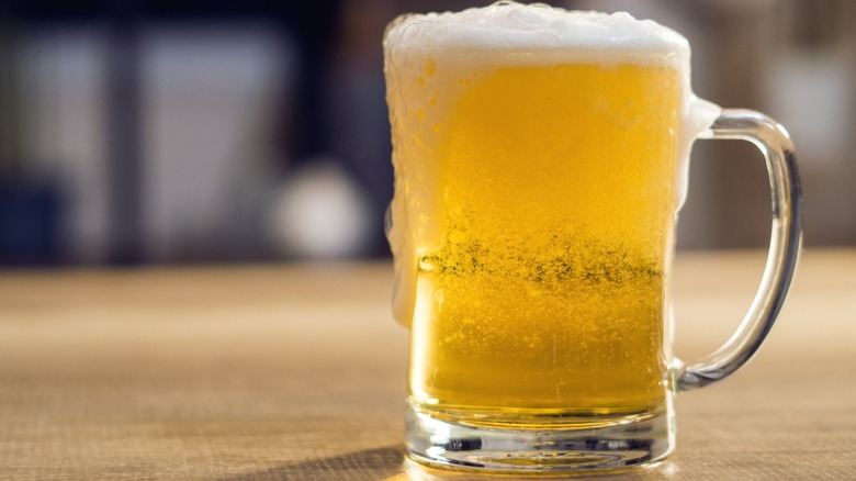 A mug of beer sitting on a wooden surface.