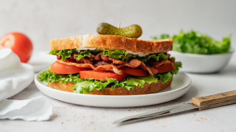 Close up of BLT sandwich on white plate garnished with a pickle