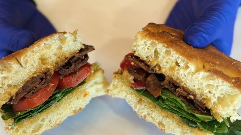 Hands wearing blue gloves holding Market on Front Vegan Avocago BLT