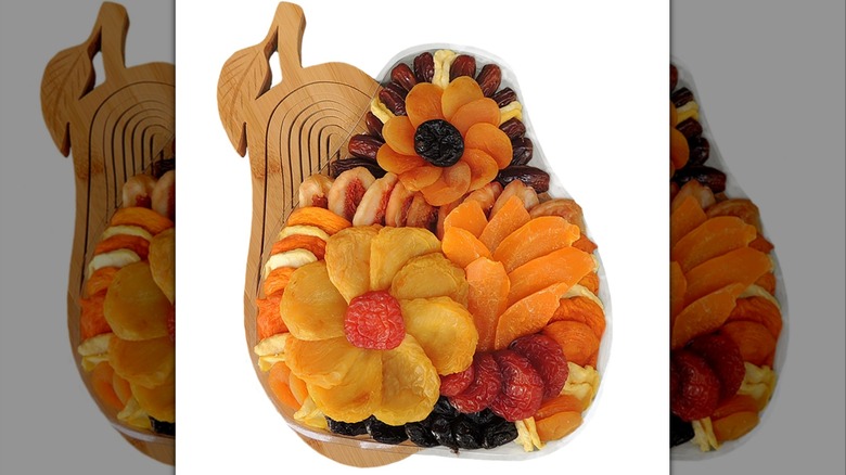 various dried fruits arranged into flowers atop a pear shaped wooden trivet