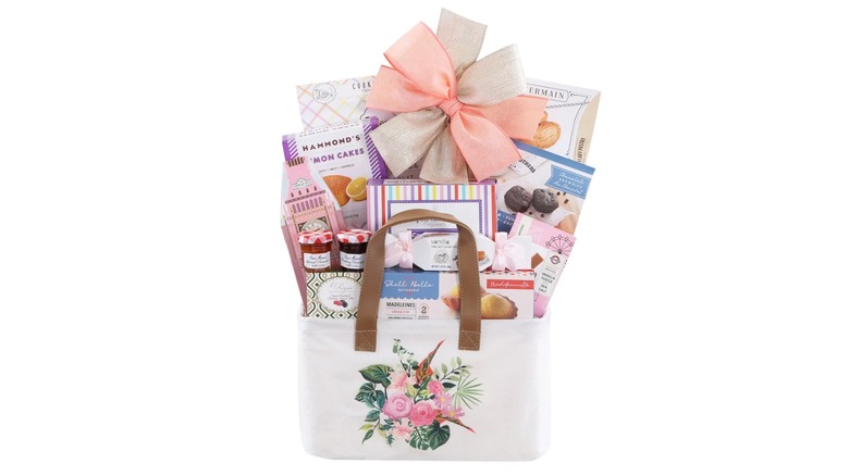 white canvas tote with a floral graphic full of boxes of treats, with food items displayed on plates in front of it and a potted pink flower displayed behind