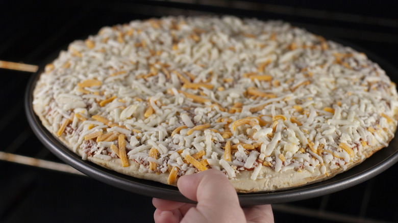 hand putting frozen pizza in oven