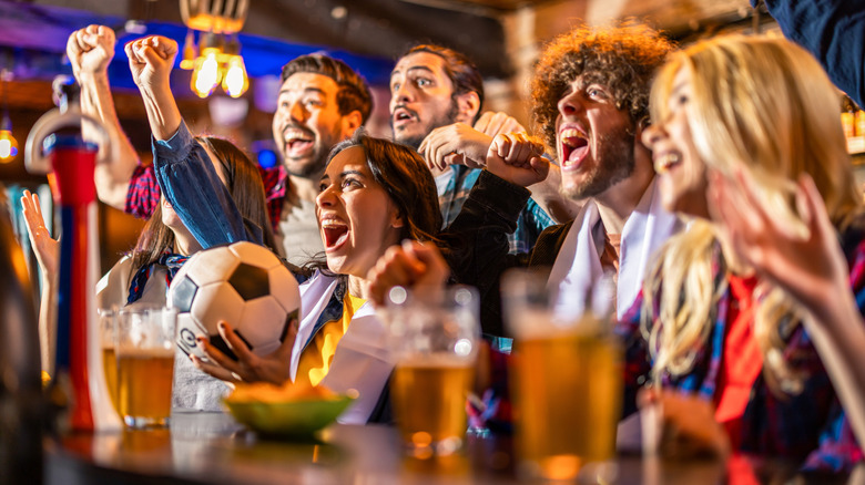 A group of young people watching soccer in bar cheering