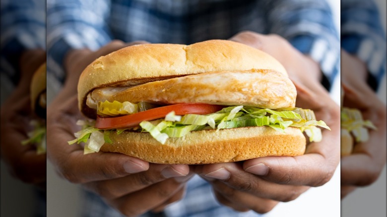 Someone holding a grilled chicken sandwich from Culver's, loaded with lettuce, tomatoes, and pickle slices
