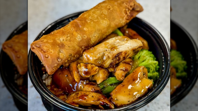 A large egg roll positioned on top of a chicken chicken teriyaki bowl from Carl's Jr.
