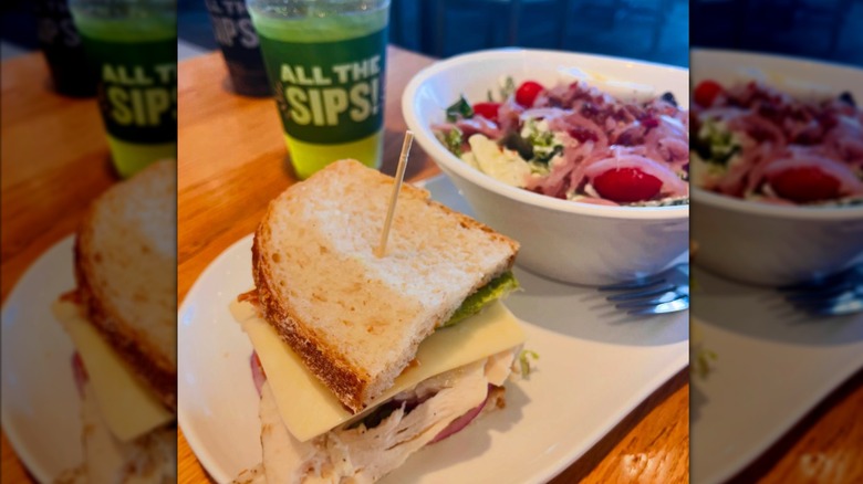 Half of a sandwich, a small salad, and a green drink positioned on a table inside Panera Bread